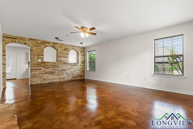 unfurnished living room with concrete flooring, arched walkways, a ceiling fan, baseboards, and visible vents