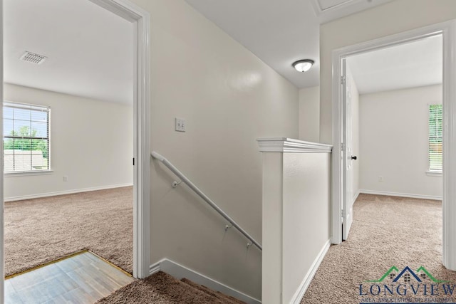 hallway featuring visible vents, carpet, baseboards, and an upstairs landing