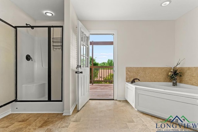 bathroom featuring baseboards, stone finish floor, a shower stall, and a garden tub
