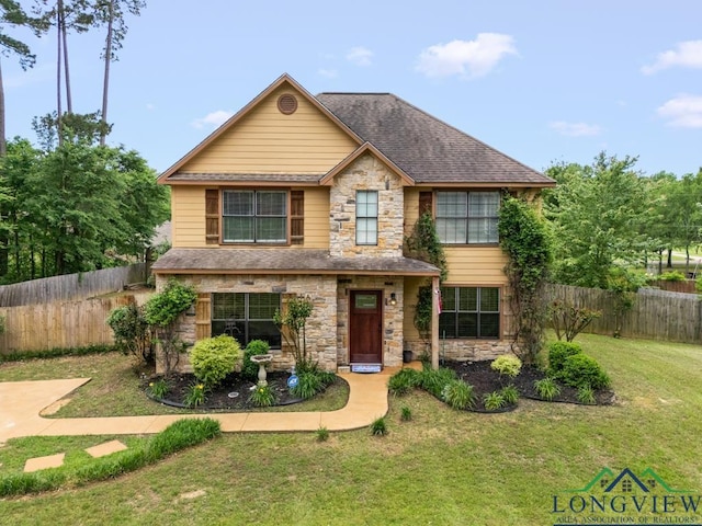 traditional-style home with a front yard, fence, a shingled roof, and stone siding
