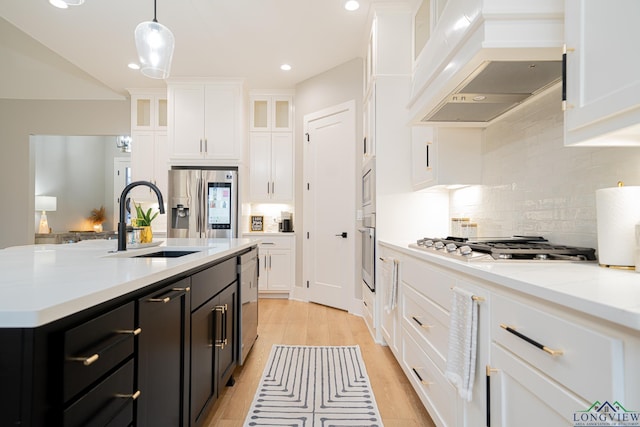 kitchen with appliances with stainless steel finishes, white cabinets, sink, a kitchen island with sink, and custom range hood