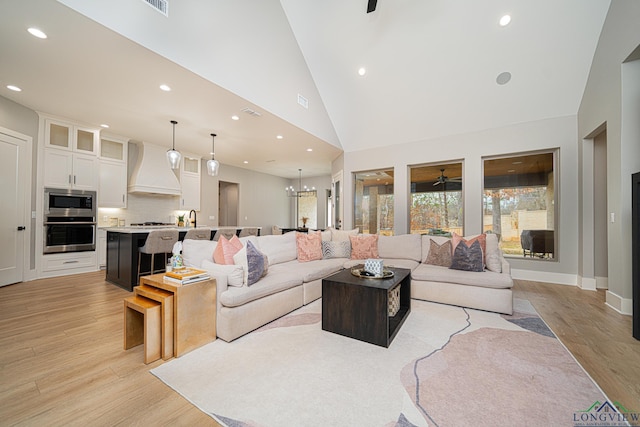 living room featuring sink, light hardwood / wood-style floors, ceiling fan with notable chandelier, and high vaulted ceiling