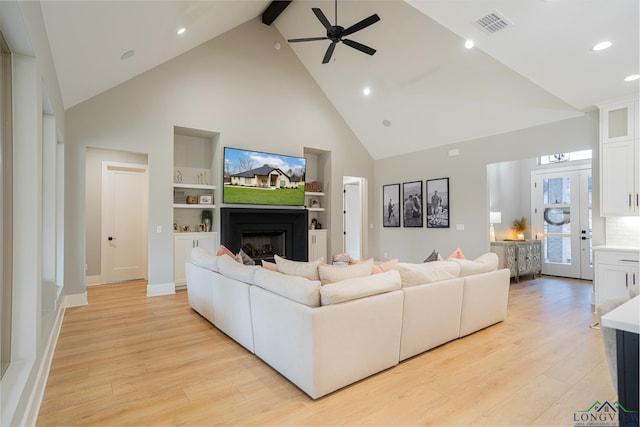 living room featuring high vaulted ceiling, built in shelves, ceiling fan, and light wood-type flooring