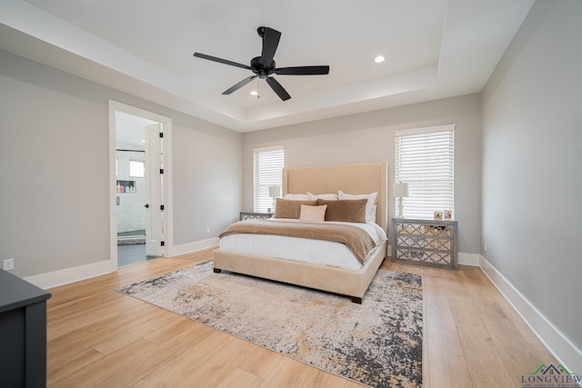 bedroom with a tray ceiling, light hardwood / wood-style flooring, and ensuite bathroom