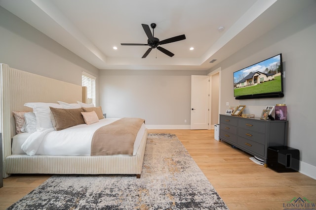 bedroom with light wood-type flooring, ceiling fan, and a tray ceiling