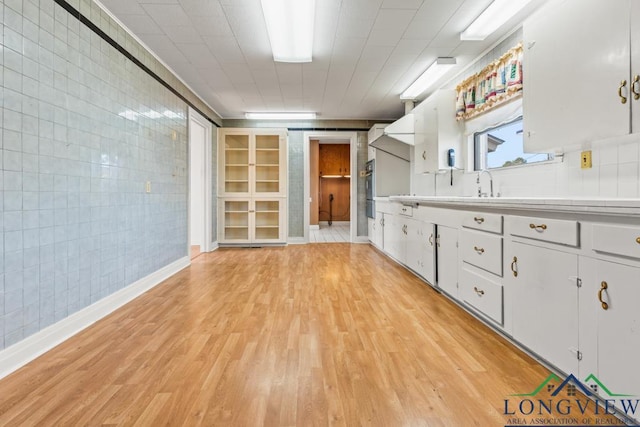 interior space featuring tile countertops, light wood-style floors, white cabinets, tile walls, and a sink