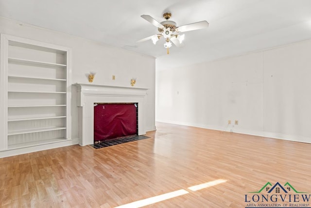 unfurnished living room featuring a fireplace with flush hearth, built in shelves, a ceiling fan, and light wood finished floors