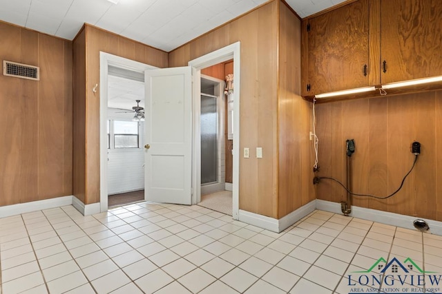 interior space with light tile patterned floors, baseboards, visible vents, ceiling fan, and wood walls