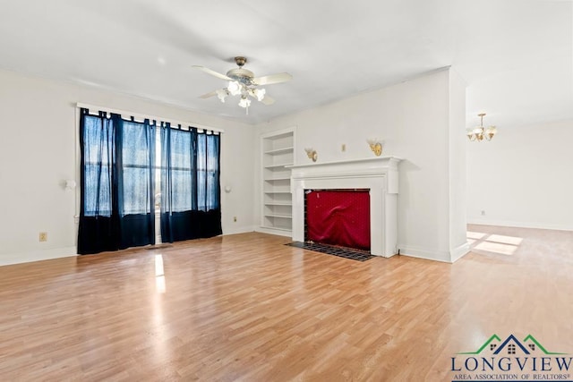 unfurnished living room with light wood-type flooring, built in shelves, a fireplace with flush hearth, and ceiling fan with notable chandelier