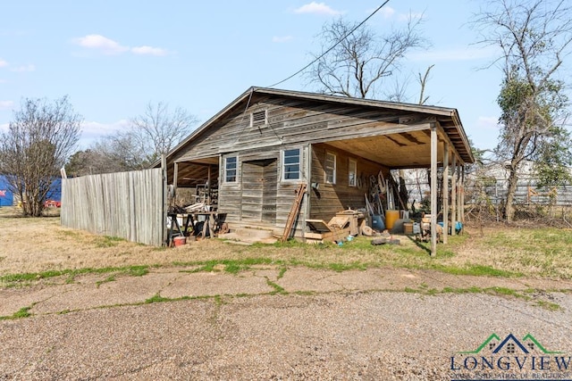 view of outdoor structure featuring an attached carport, fence, driveway, and an outdoor structure