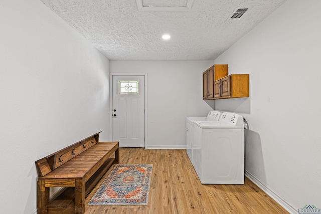 laundry room with washing machine and clothes dryer, cabinets, a textured ceiling, and light wood-type flooring