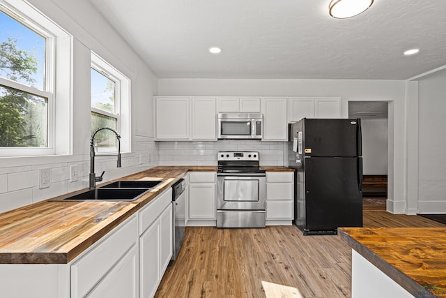 kitchen featuring decorative backsplash, appliances with stainless steel finishes, sink, white cabinets, and butcher block countertops