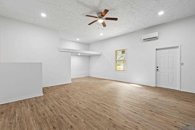 unfurnished living room with a wall mounted air conditioner, ceiling fan, hardwood / wood-style floors, and a textured ceiling