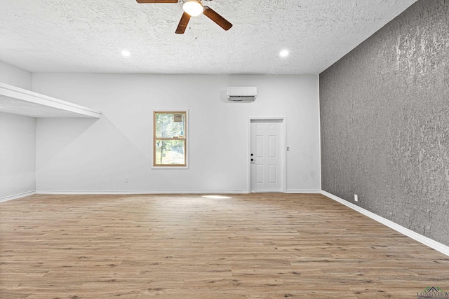 spare room with a wall mounted air conditioner, wood-type flooring, a textured ceiling, and ceiling fan