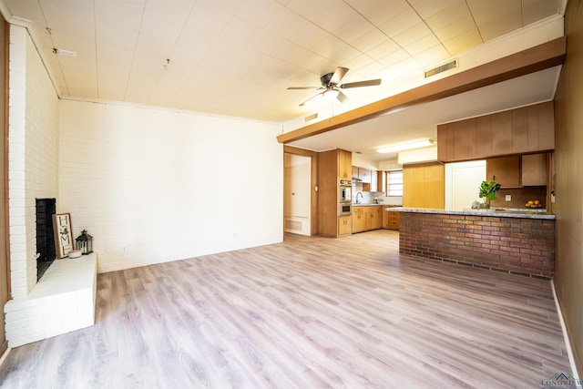 unfurnished living room featuring a fireplace, brick wall, ceiling fan, and light wood-type flooring