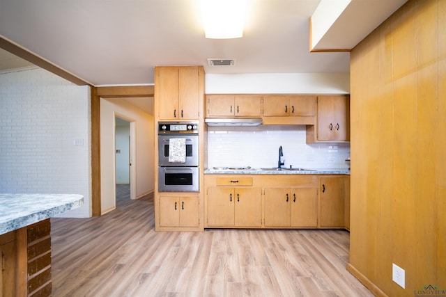 kitchen with light hardwood / wood-style floors, stainless steel double oven, decorative backsplash, light brown cabinetry, and sink