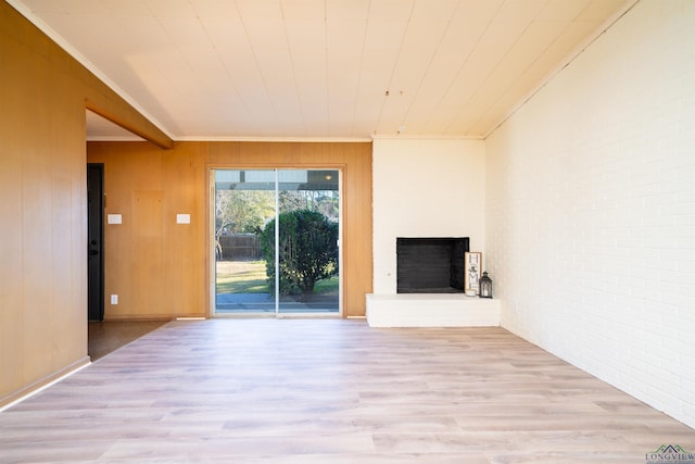 unfurnished living room featuring brick wall, wood walls, ornamental molding, a brick fireplace, and light hardwood / wood-style flooring