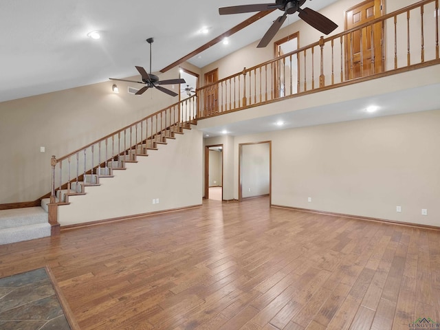 unfurnished living room featuring hardwood / wood-style floors, ceiling fan, and a high ceiling