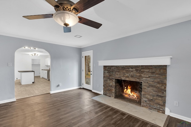 unfurnished living room with crown molding, ceiling fan, a stone fireplace, and hardwood / wood-style floors