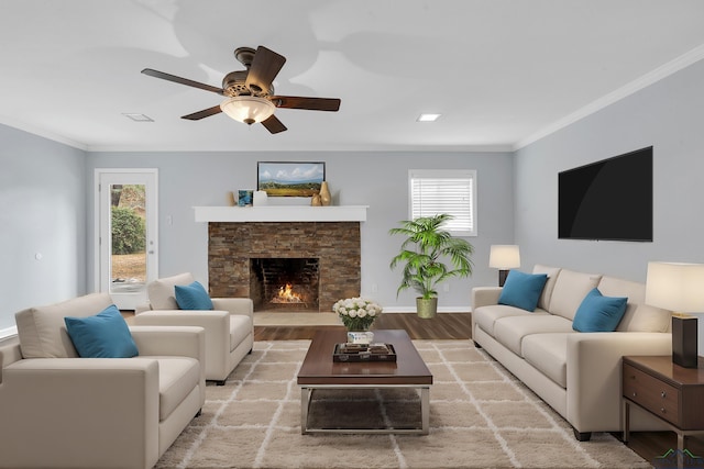 living room featuring a stone fireplace, wood-type flooring, ornamental molding, and ceiling fan