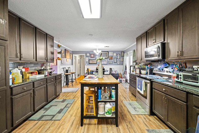 kitchen with dark brown cabinetry, stainless steel appliances, crown molding, dark stone countertops, and light hardwood / wood-style floors