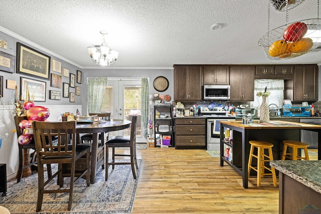 kitchen with appliances with stainless steel finishes, french doors, ornamental molding, dark brown cabinets, and a notable chandelier