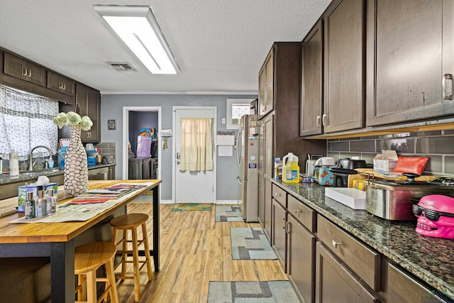 kitchen featuring backsplash, dark stone counters, a textured ceiling, light hardwood / wood-style floors, and washer and dryer