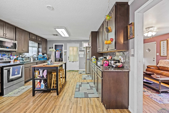 kitchen featuring dark stone counters, dark brown cabinets, a textured ceiling, stainless steel appliances, and light hardwood / wood-style floors