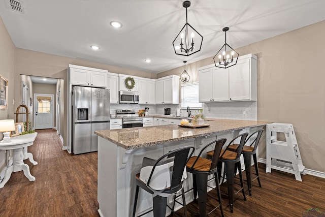 kitchen featuring hanging light fixtures, stainless steel appliances, a breakfast bar, and white cabinets