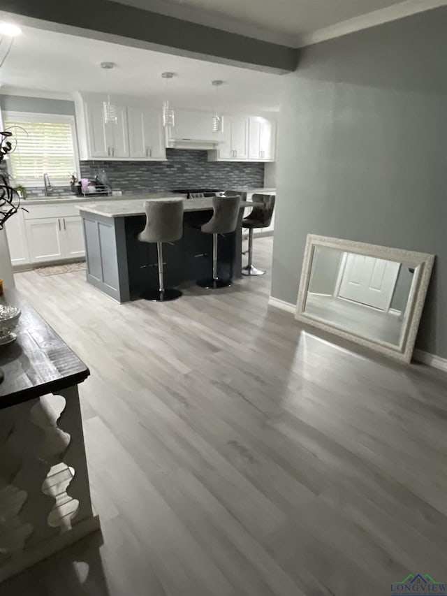 kitchen with pendant lighting, a kitchen breakfast bar, light hardwood / wood-style flooring, a kitchen island, and white cabinetry