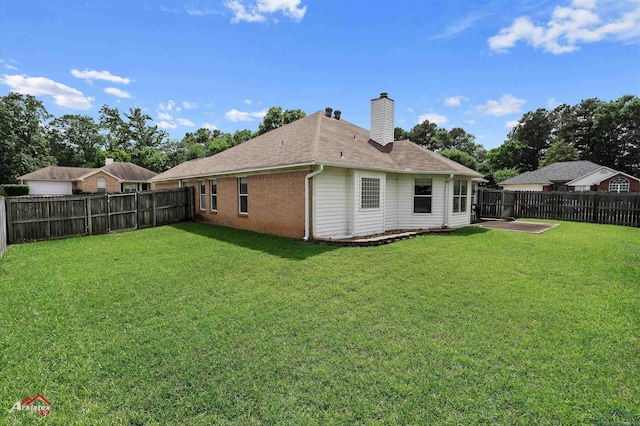 back of house with a fenced backyard, a chimney, and a yard