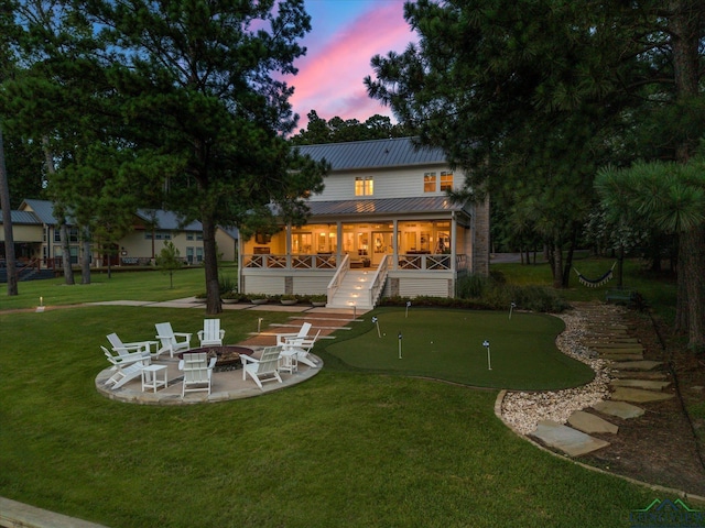 378 Cypress Creek Dr, Mount Vernon, TX 75457 - back of house at dusk with an area to practice putting, a fire pit, a patio, a lawn, and a metal roof