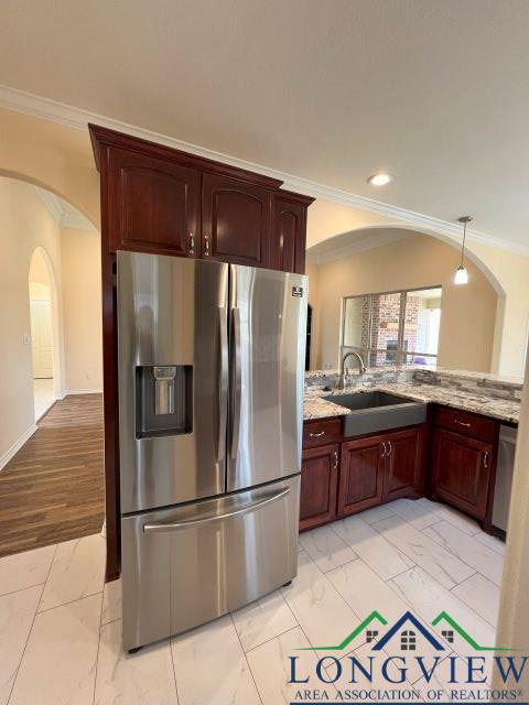 kitchen with decorative light fixtures, sink, stainless steel appliances, crown molding, and light stone countertops