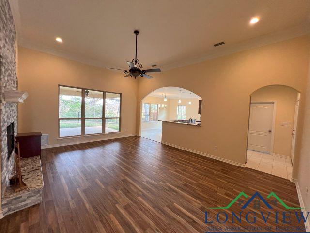 unfurnished living room featuring dark hardwood / wood-style flooring, a stone fireplace, crown molding, and ceiling fan