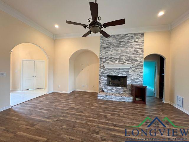 unfurnished living room with dark wood-type flooring, ceiling fan, crown molding, and a stone fireplace