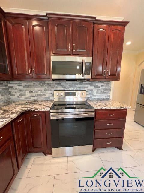 kitchen featuring crown molding, stainless steel appliances, light stone countertops, and backsplash