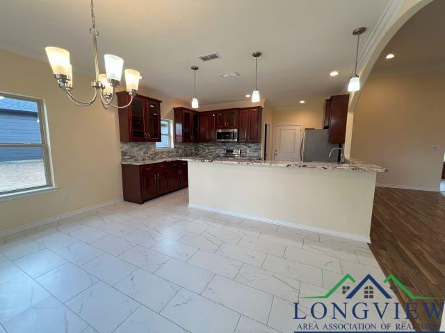 kitchen with appliances with stainless steel finishes, hanging light fixtures, light stone countertops, decorative backsplash, and kitchen peninsula