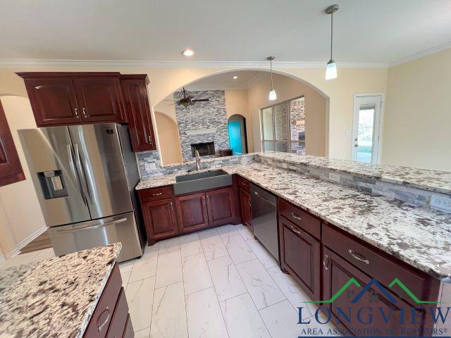 kitchen featuring sink, hanging light fixtures, stainless steel appliances, a fireplace, and light stone countertops