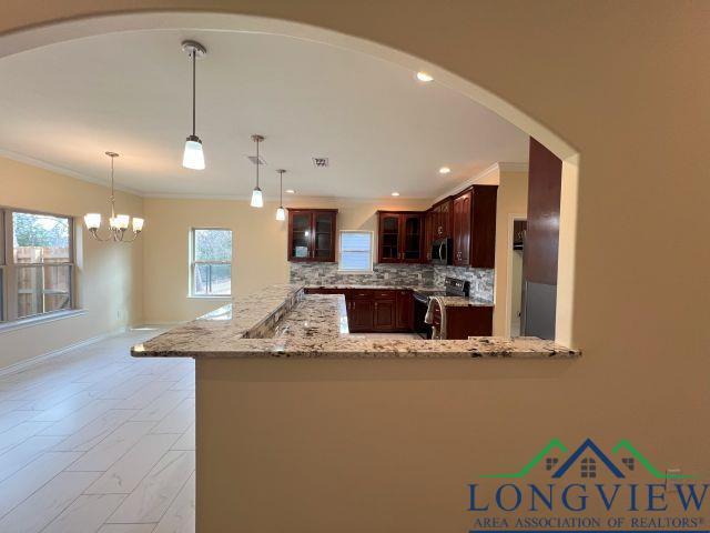 kitchen featuring hanging light fixtures, appliances with stainless steel finishes, light stone counters, and kitchen peninsula