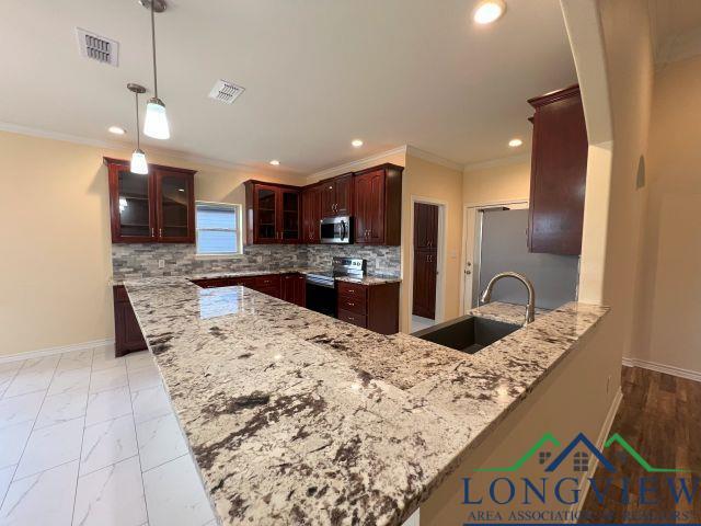 kitchen featuring appliances with stainless steel finishes, sink, hanging light fixtures, kitchen peninsula, and light stone countertops