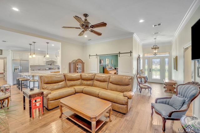 living room with light wood-type flooring, a barn door, ceiling fan, and crown molding