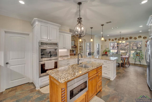 kitchen featuring light stone countertops, sink, stainless steel appliances, a kitchen island with sink, and white cabinets