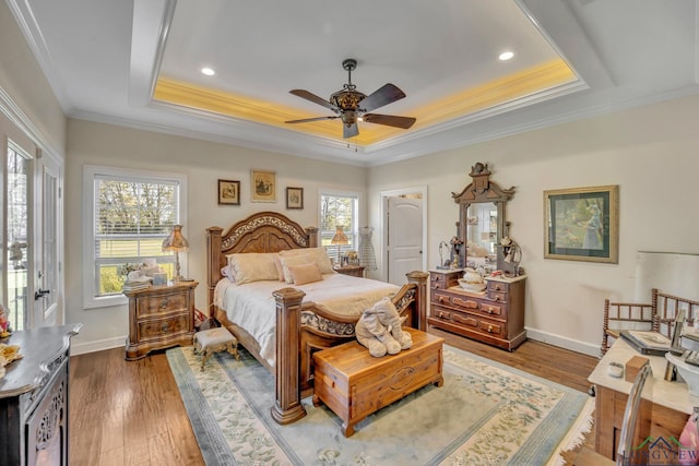 bedroom with ceiling fan, hardwood / wood-style floors, a tray ceiling, multiple windows, and ornamental molding