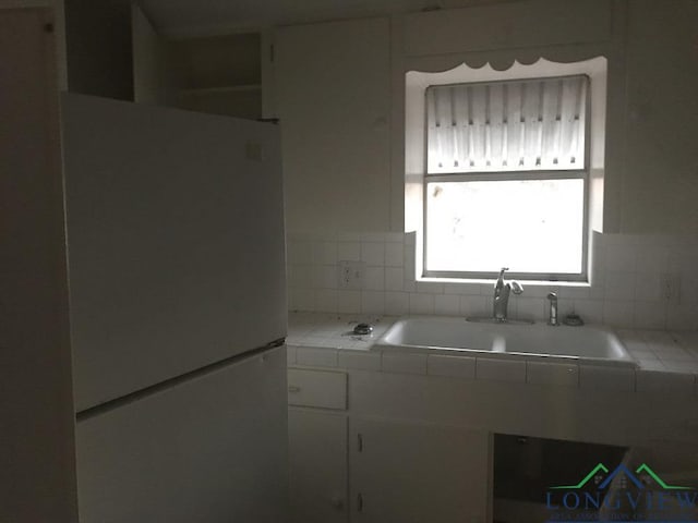 kitchen with sink, white cabinetry, tile countertops, white fridge, and backsplash