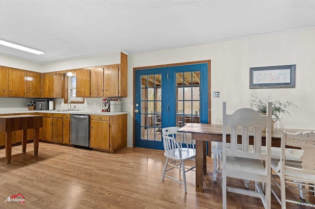 kitchen with a sink, light countertops, stainless steel dishwasher, brown cabinets, and light wood finished floors