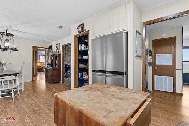 kitchen with light wood finished floors, visible vents, hanging light fixtures, freestanding refrigerator, and white cabinetry