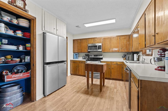 kitchen with a sink, light countertops, appliances with stainless steel finishes, light wood-type flooring, and brown cabinetry