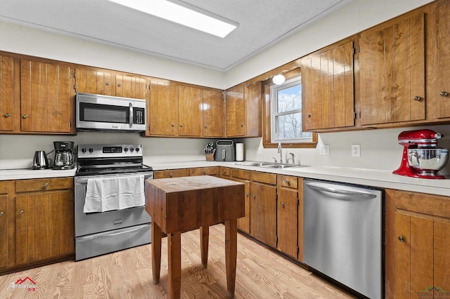 kitchen with light countertops, appliances with stainless steel finishes, brown cabinetry, a sink, and light wood-type flooring