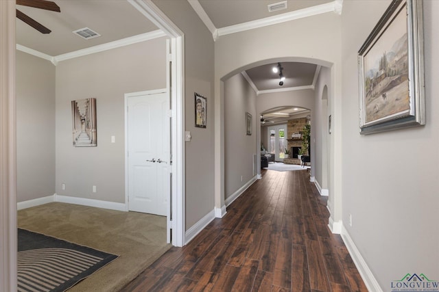 corridor with crown molding, arched walkways, dark wood-style floors, and visible vents
