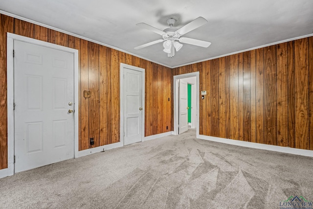 interior space featuring carpet flooring, ceiling fan, ornamental molding, and wood walls